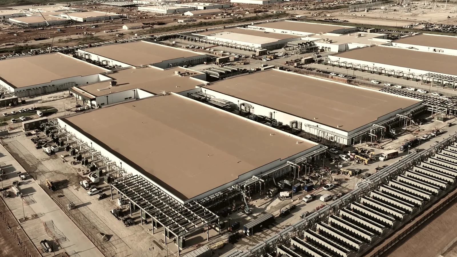 Aerial view of rows of identical hyperscale data center halls with banks of generators along one flank.