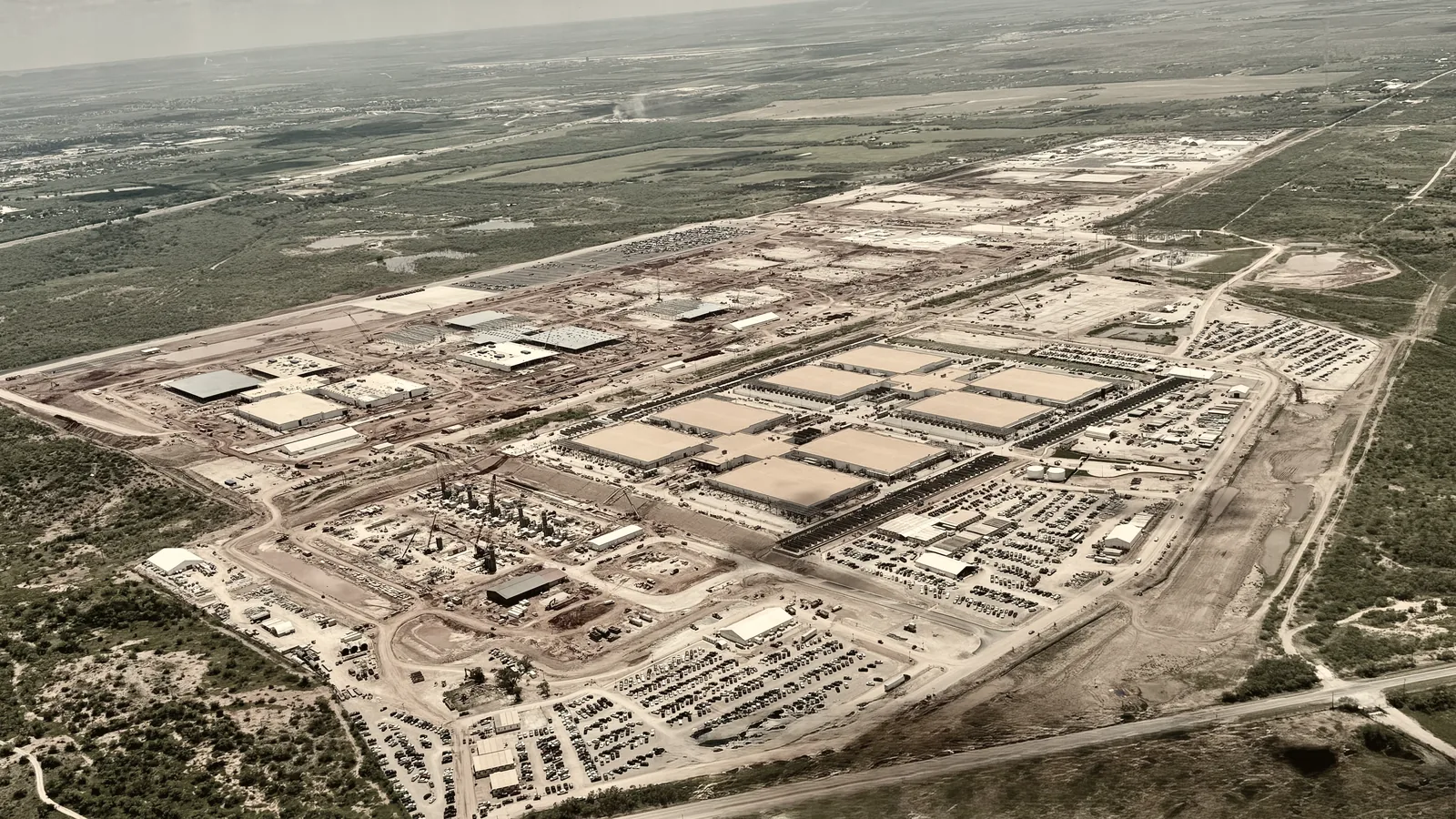 Aerial view of a hyperscale data center campus carved out of farmland, with green fields still visible at its edge.